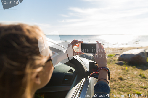 Image of happy young woman in car with smartphone at sea