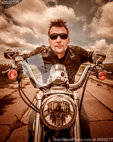 Image of Biker in a leather jacket riding a motorcycle on the road