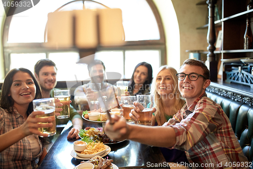 Image of happy friends with selfie stick at bar or pub