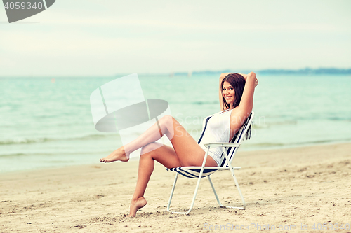 Image of smiling young woman sunbathing in lounge on beach