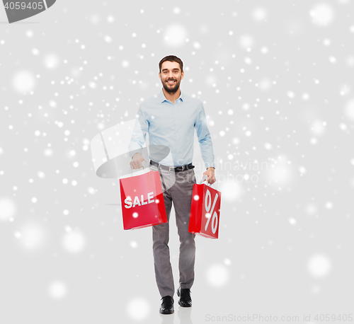 Image of smiling man with red shopping bags over snow