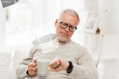 Image of senior man with coffee looking at wristwatch