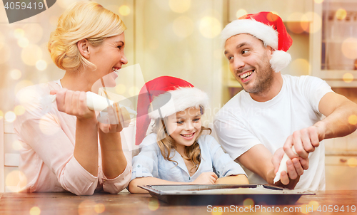 Image of happy family in santa helper hats making cookies