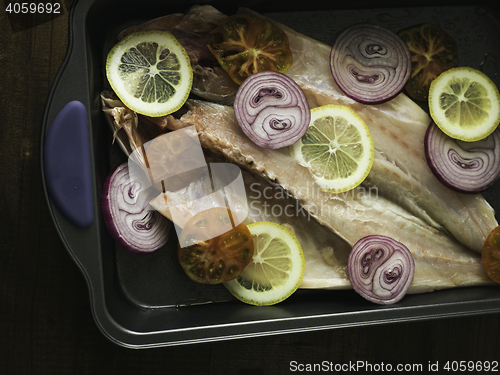 Image of raw sea bass with lemon, onion and tomato ready