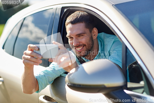 Image of happy smiling man with smartphone driving in car