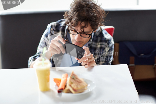 Image of man with smartphone photographing food at cafe
