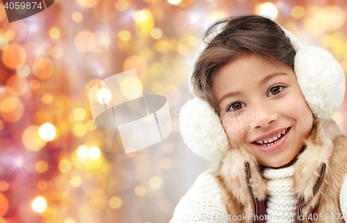 Image of happy little girl in earmuffs over holidays lights