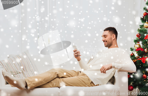 Image of smiling man with smartphone at home for christmas