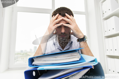 Image of sad businessman with stack of folders at office