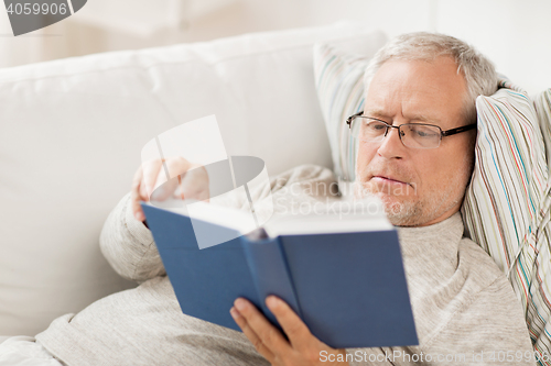 Image of senior man lying on sofa and reading book at home