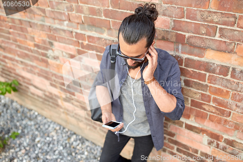 Image of man with earphones, smartphone and bag on street