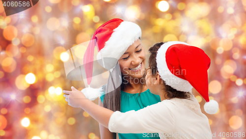 Image of happy little girl in santa hat hugging her mother