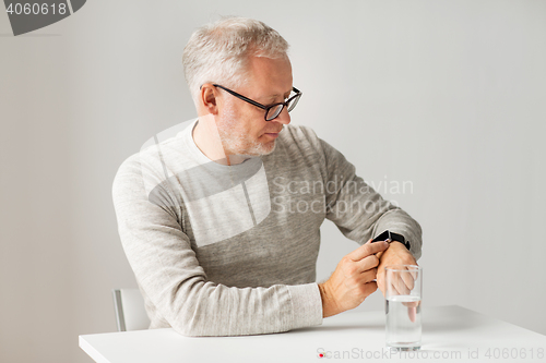 Image of senior man with water and pill looking at watch