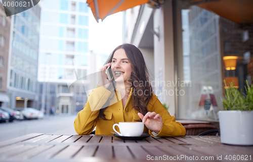 Image of happy woman calling on smartphone at city cafe