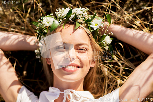 Image of happy woman in wreath of flowers lying on straw