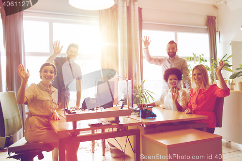 Image of happy creative team waving hands in office