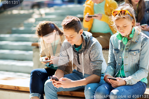 Image of teenage friends with smartphones outdoors