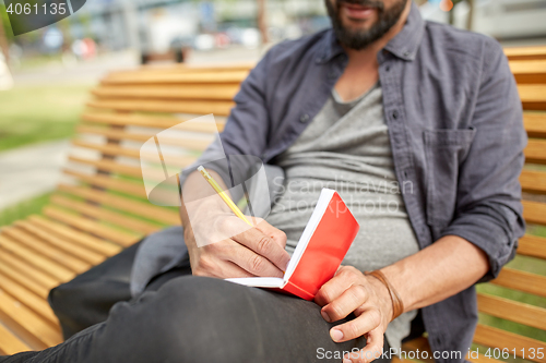 Image of close up of man writing to notebook on city street