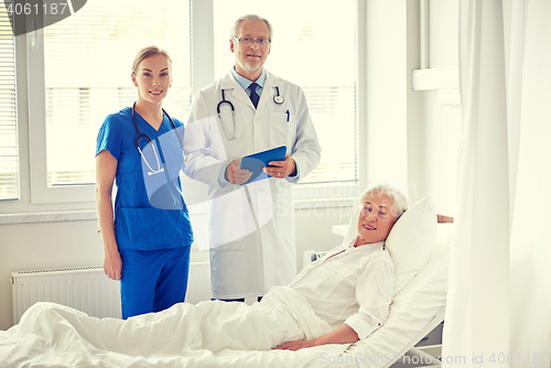 Image of doctor and nurse visiting senior woman at hospital