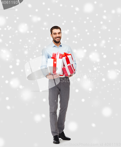 Image of happy young man holding christmas gifts over snow