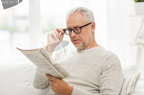 Image of senior man in glasses reading newspaper at home