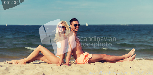 Image of happy couple in swimwear sitting on summer beach