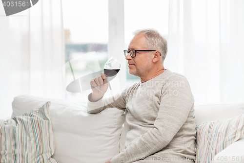 Image of senior man drinking red wine from glass at home