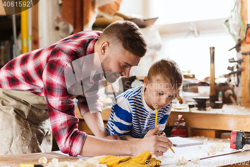 Image of happy father and son with blueprint at workshop