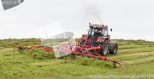 Image of Farmer uses tractor to spread hay on the field