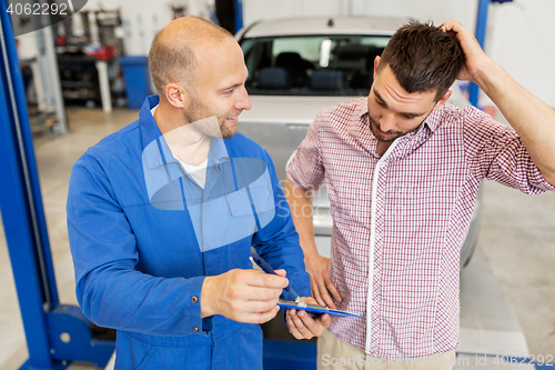 Image of auto mechanic with clipboard and man at car shop