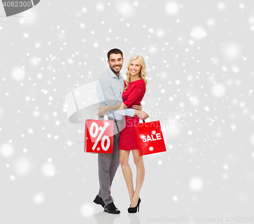 Image of happy couple with red shopping bags over snow