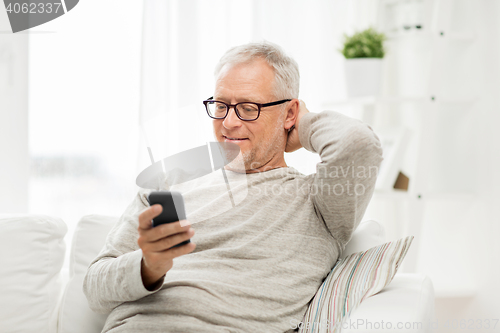 Image of happy senior man texting on smartphone at home