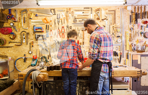 Image of father and little son with wood plank at workshop