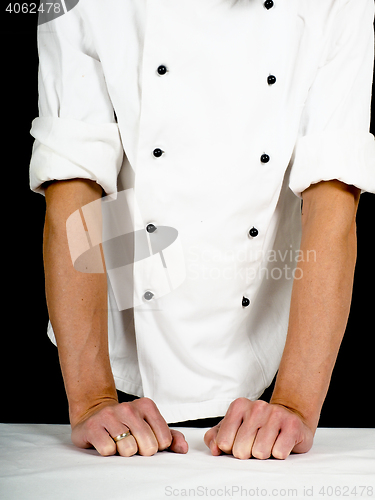 Image of Professional chef leaning firmly onto a table with white cover