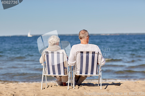 Image of senior couple sitting on chairs at summer beach