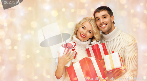 Image of happy couple in sweaters holding christmas gifts