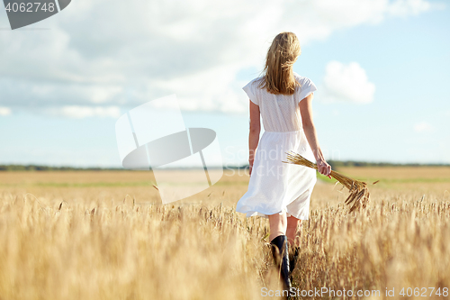 Image of young woman with cereal spikelets walking on field