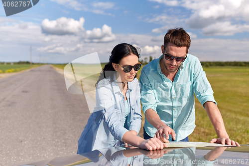 Image of happy man and woman with road map on car hood