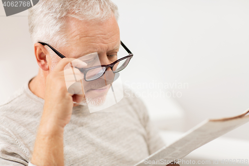 Image of close up of old man in glasses reading newspaper