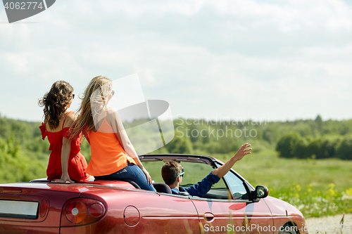 Image of happy friends driving in cabriolet car at country
