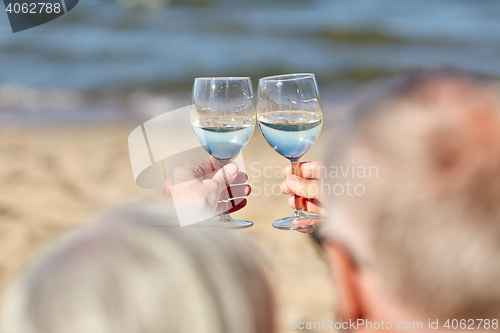 Image of happy senior couple drinking wine on summer beach