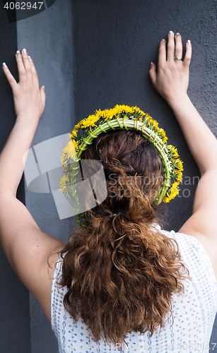Image of Woman stretching against a grey wall with a flower wreath in bea