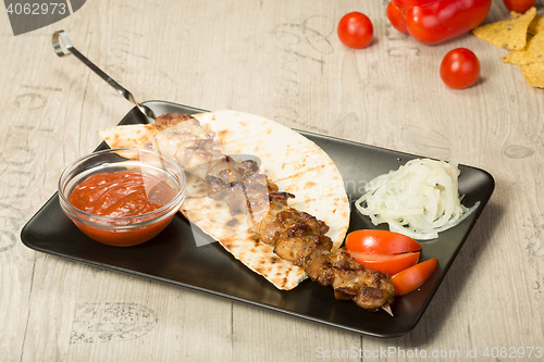 Image of shashlik. kebab skewer, black rectangular plate. sauce and onions