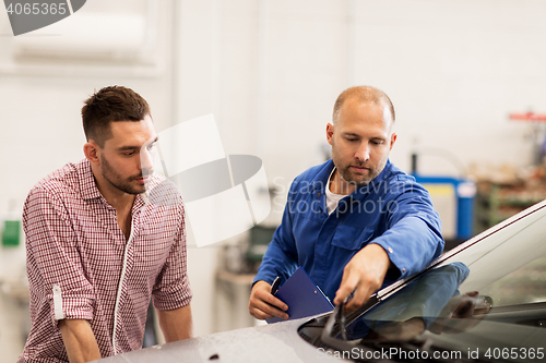 Image of auto mechanic with clipboard and man at car shop