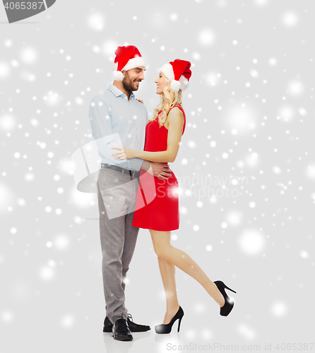 Image of happy couple in santa hats hugging over snow