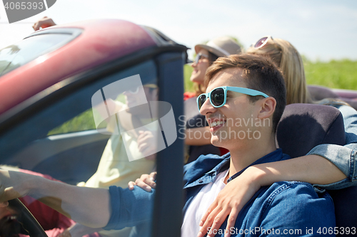 Image of happy friends driving in cabriolet car at country