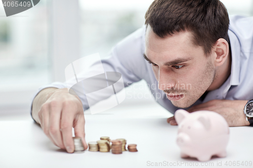 Image of businessman with piggy bank and coins at office