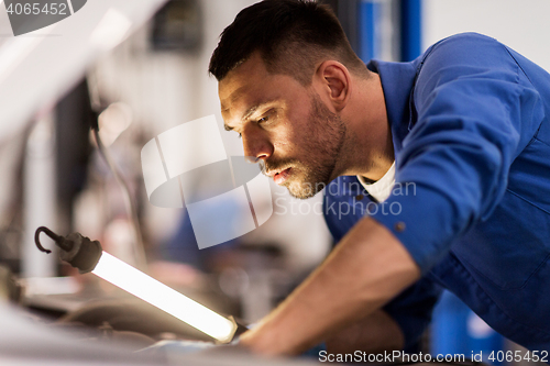 Image of mechanic man with lamp repairing car at workshop