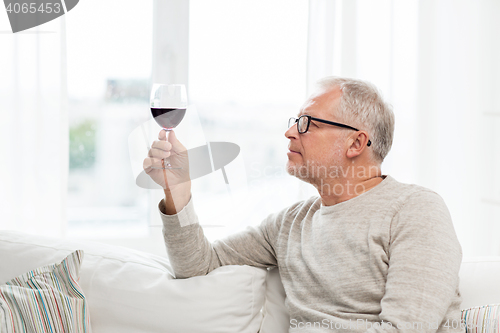 Image of senior man drinking red wine from glass at home