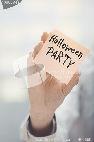 Image of Woman holding adhesive note with Halloween party text